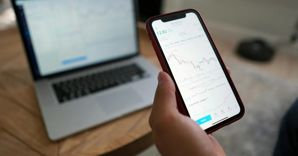 Agibank AGBK11: Investidor analisa ações em celular e laptop após divulgação de resultados financeiros.