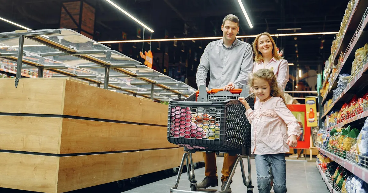 Família feliz no supermercado, ilustrando o impacto da inflação e alta nos preços de alimentos em 2027.