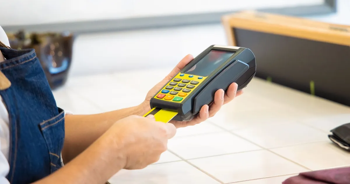 Mãos usam máquina POS com cartão de crédito, simbolizando acesso a crédito e juros menores para empresas no BC.