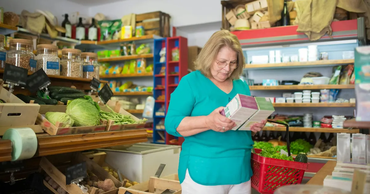 Varejo em Portugal: idosa observa produto em mercado. Sinais mistos na economia, impacto no agro e varejo.