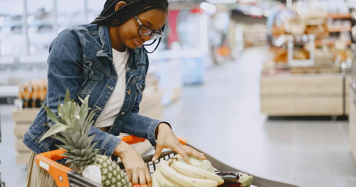 Mulher compra alimentos essenciais em supermercado. Ilustra o impacto da inflação e aumento da cesta básica na vida em SP.