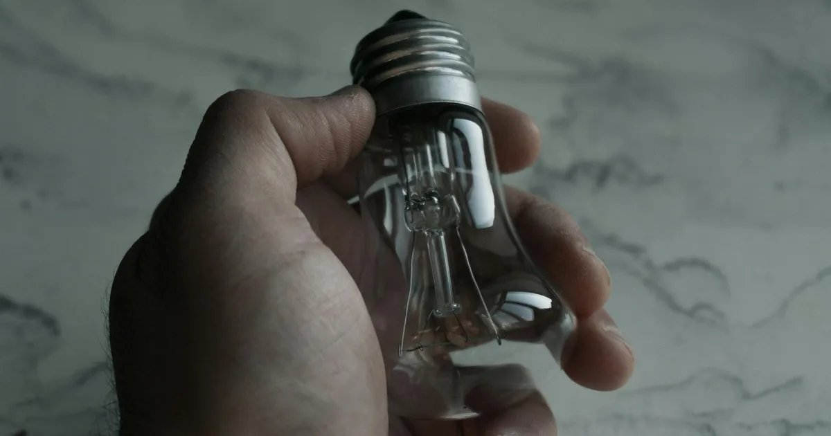 Mão segura lâmpada apagada; reajustes de tarifas de energia pela Aneel elevam o custo de vida e a inflação.