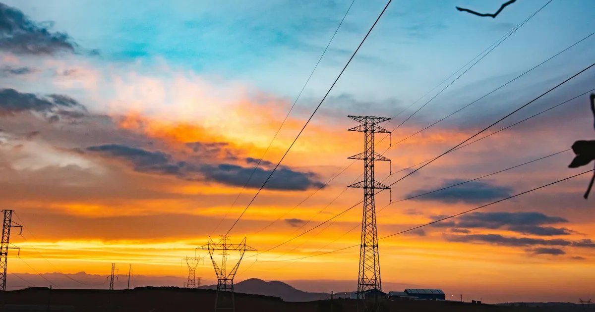 Contas de luz mais caras? Silhueta de torres de energia no pôr do sol. Entenda o custo da energia no Brasil.