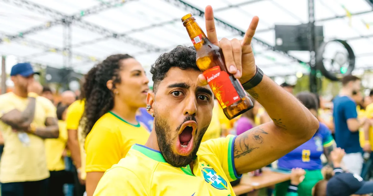 Torcedor brasileiro celebra PIB subindo e Copa do Mundo em bar, refletindo agitação do mercado financeiro.
