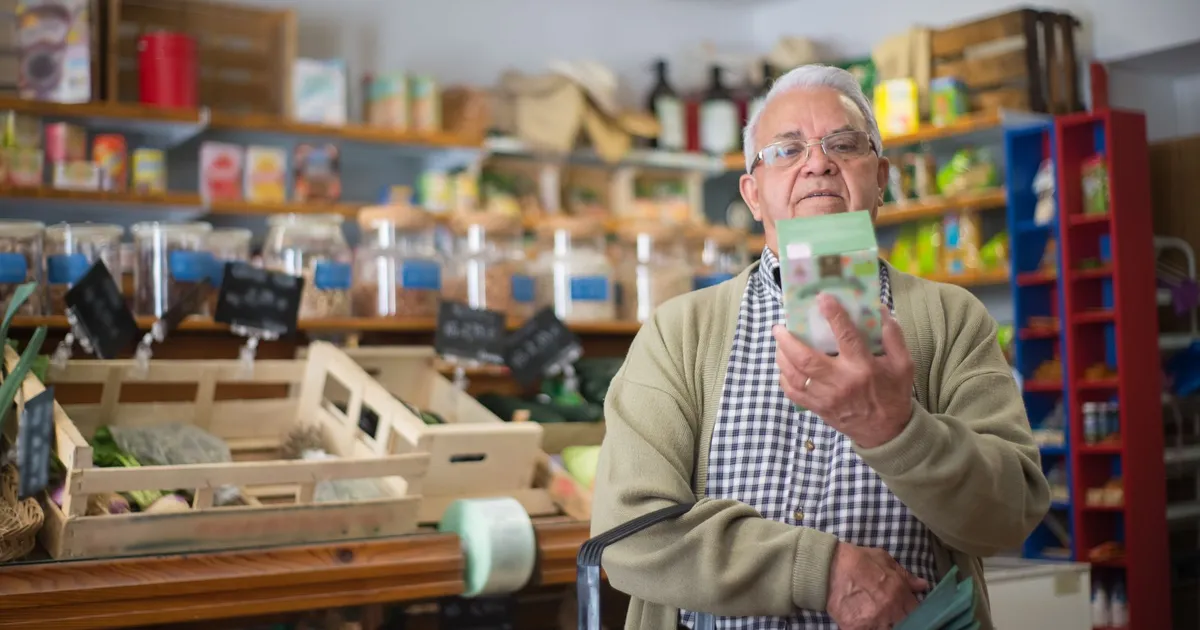 Idoso avalia produtos no supermercado, reflexo do impacto do El Niño e inflação na rotina de compras do brasileiro.