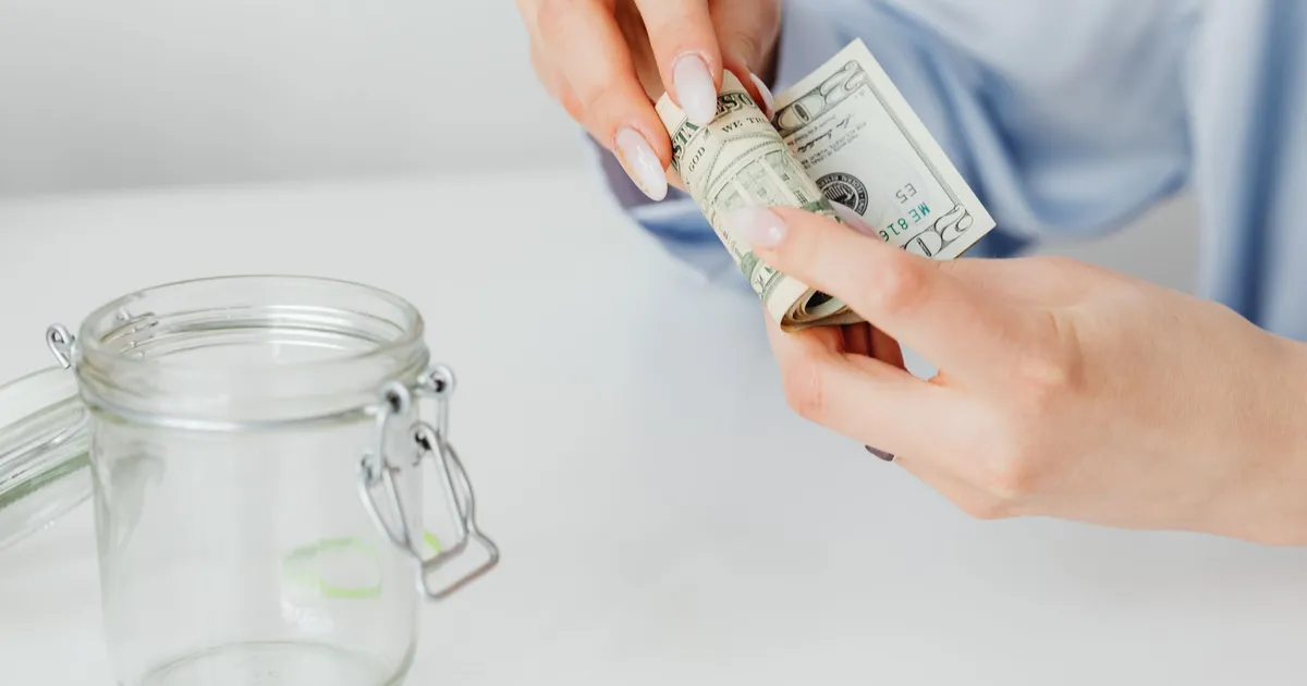 Mulher enrola notas de dólar ao lado de cofre, simbolizando distribuição de R$ 13 bi em dividendos do FGTS.