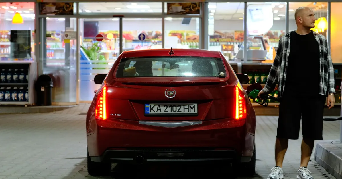 Caminhoneiro abastecendo carro vermelho em posto de gasolina à noite; frete, etanol e gasolina em pauta.