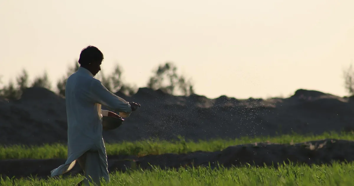 Fazendeiro com fertilizantes sob pôr do sol, impactado por guerra no Irã.