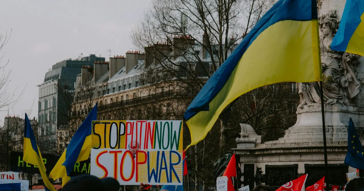 Manifestantes em Paris com bandeiras da Ucrânia pedem paz, refletindo impacto da Guerra na Ucrânia na Economia Global.