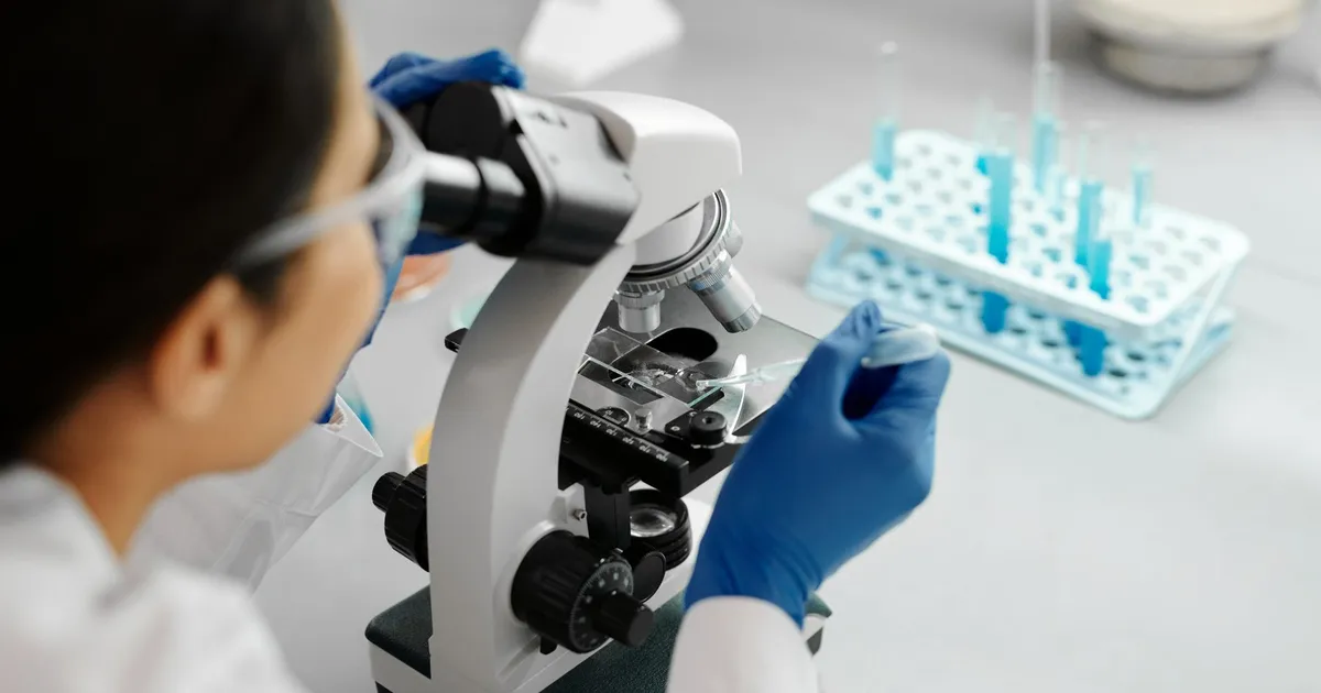 Pesquisador em laboratório com microscópio e conta-gotas, alusivo à pesquisa de novo medicamento da Hypera.
