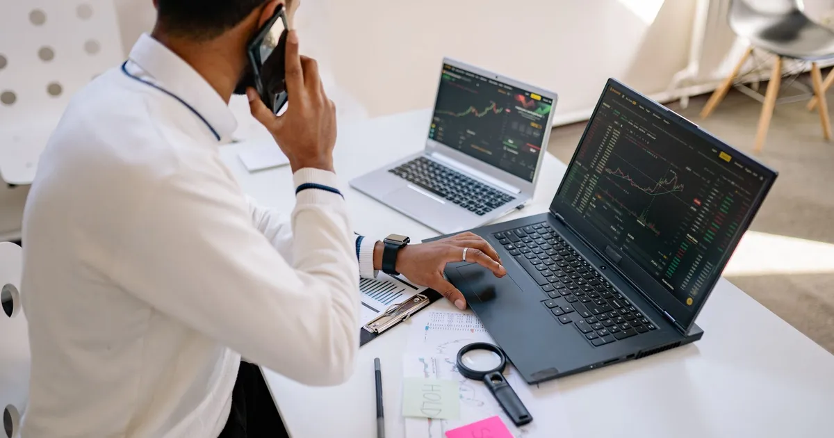 Homem analisa Ibovespa, inflação e dólar em laptops com gráficos financeiros, refletindo negociações no mercado.