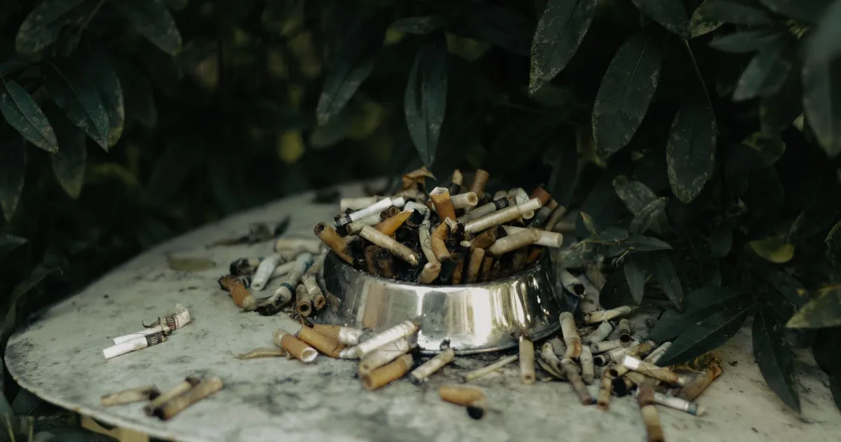 Filtros de cigarro em cinzeiro, símbolo do Imposto Seletivo e saúde pública na Reforma Tributária.