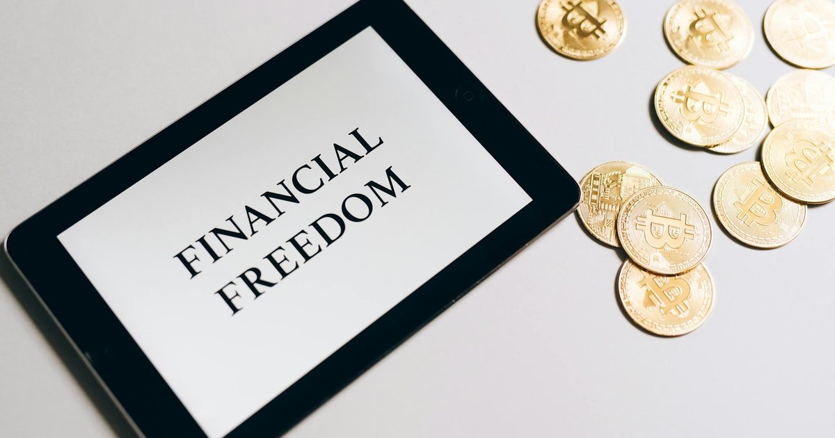 Tablet exibe 'Independência Financeira 2026' com bitcoins dourados ao lado.