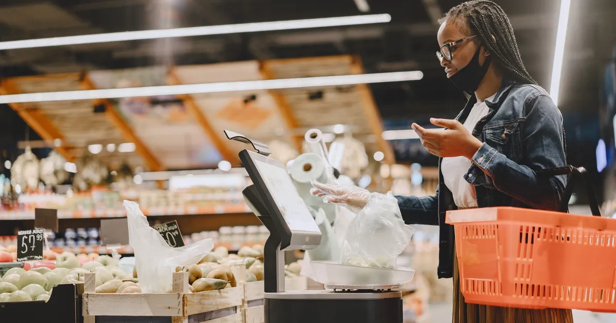Mulher de máscara compra alimentos em supermercado, refletindo a desaceleração da inflação e o tímido alívio no bolso.