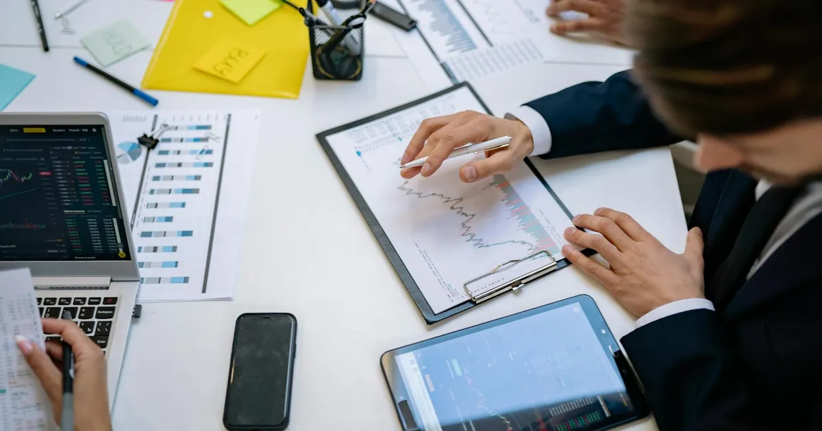 Análise de resultados JBS e Ser Educacional em escritório. Balanços, dividendos e dados financeiros em tablets.