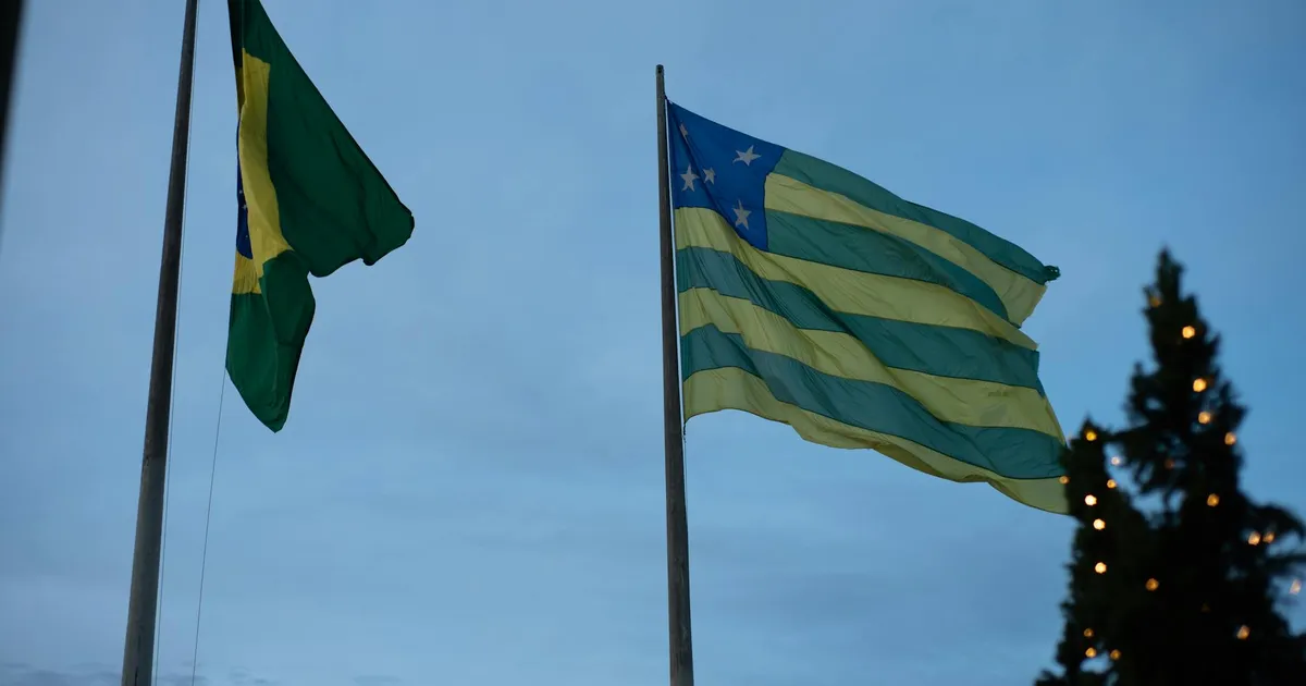Bandeiras do Brasil e Goiás no crepúsculo, com luzes. Reflete a política externa de Lula e os atritos com os EUA.