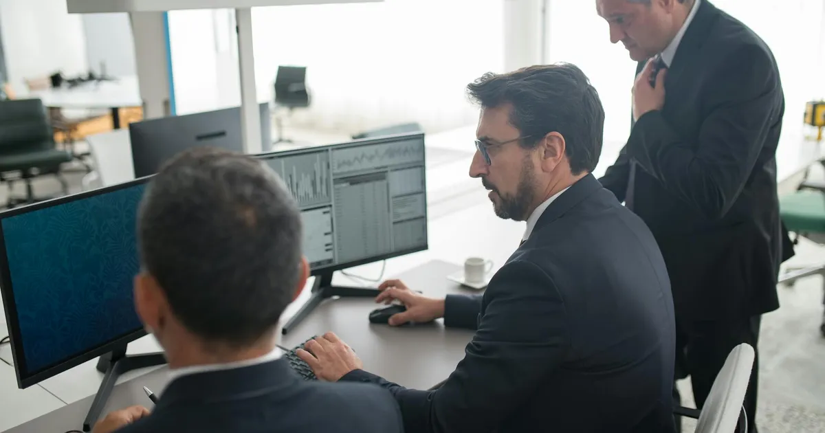 Analistas em escritório moderno monitoram tendências e dados do mercado financeiro, como ações de Braskem e Itaú.