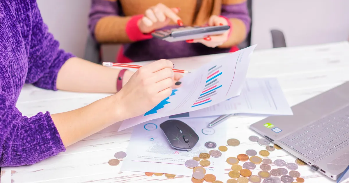 Mulheres analisam gráficos financeiros no escritório, indicando tendências de mercado e investimentos para julho.