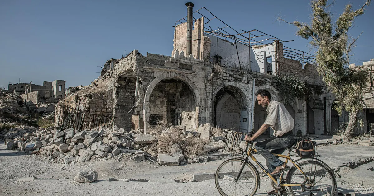 Homem de bicicleta em Aleppo, Síria, símbolo de resiliência em meio a tensões globais e impacto do preço do petróleo.