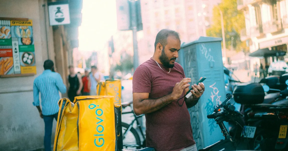 Entregador de app usa celular ao lado da bicicleta. Trabalho em aplicativos e a nova lei no Congresso.