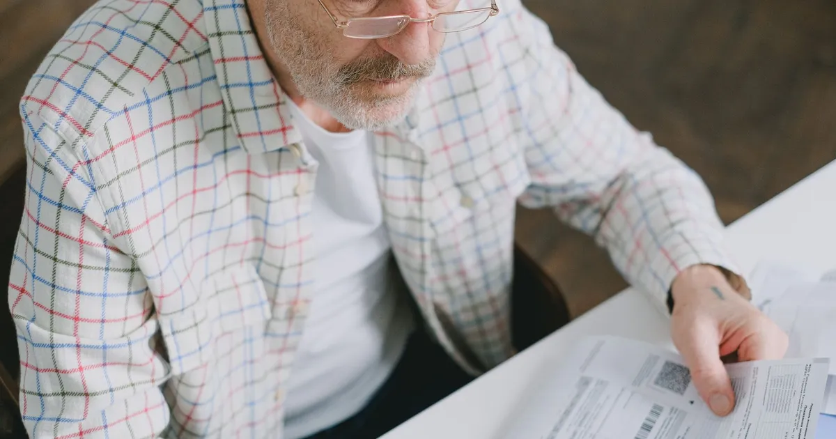 Homem idoso foca em documentos, refletindo sobre o fim da Revisão da Vida Toda no INSS.