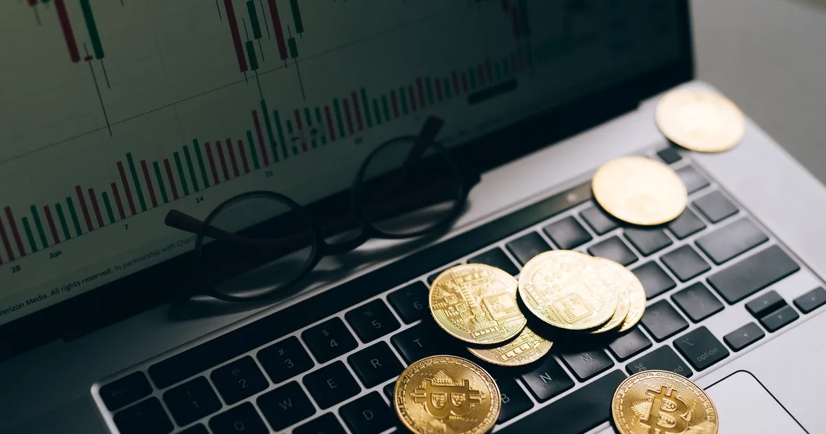 Bitcoins dourados em teclado de laptop com gráfico de mercado, simbolizando especulação de ouro e Fed hawkish.