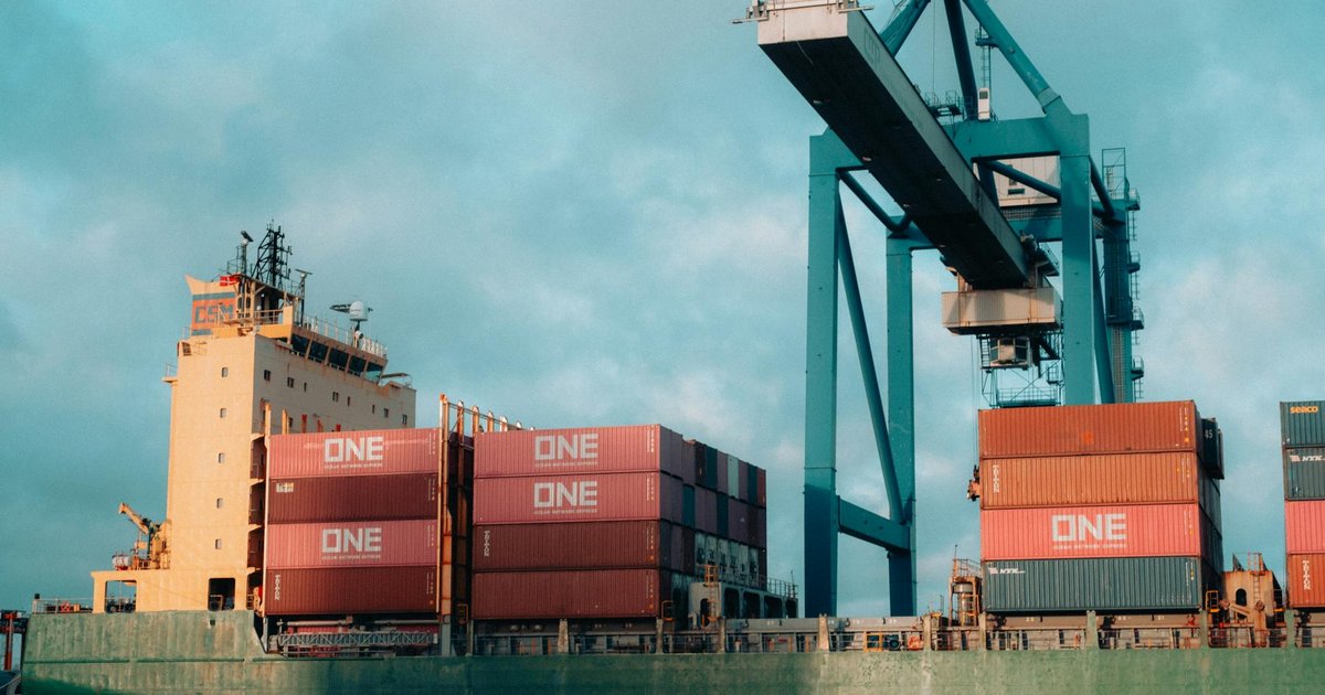Navio cargueiro gigante com contêineres coloridos em porto industrial movimentado, aludindo à regulação ANTAQ Web3.